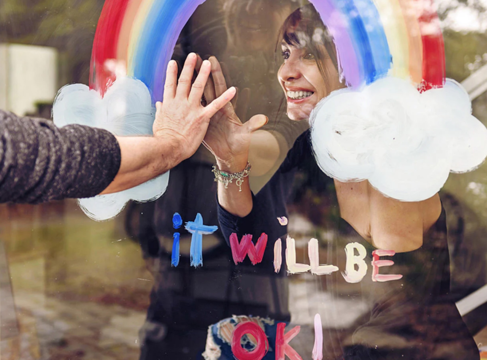 A photo of two women greeting each other through the window